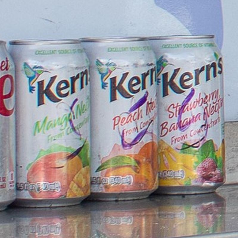 Three cans of cold Kern’s Mango, Peach, and Strawberry Banana nectar carbonated fruit drinks, lined up on the food truck trailer’s steel counter.