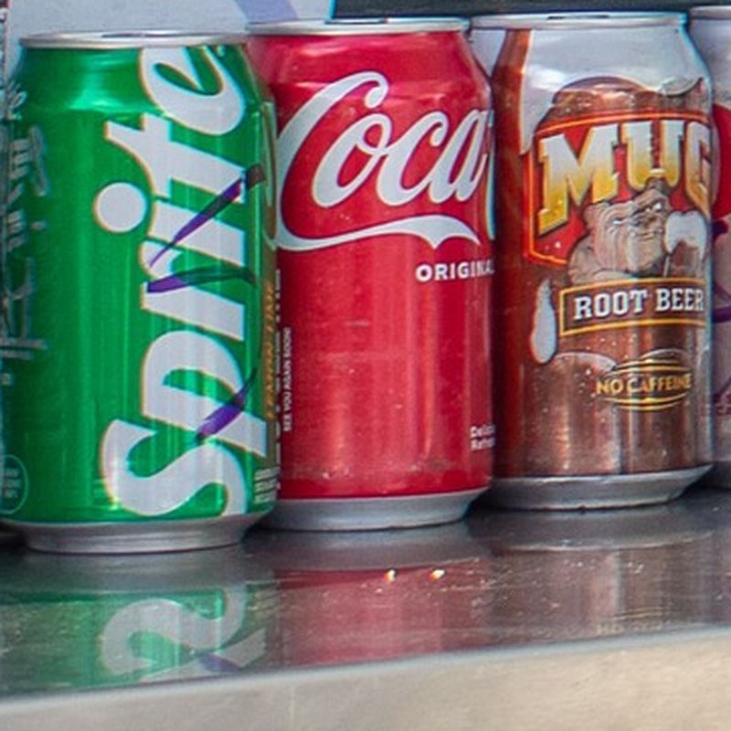 Three cans of cold Sprite, Coca-Cola, and Mug Root Beer, lined up on the food truck trailer’s steel counter.