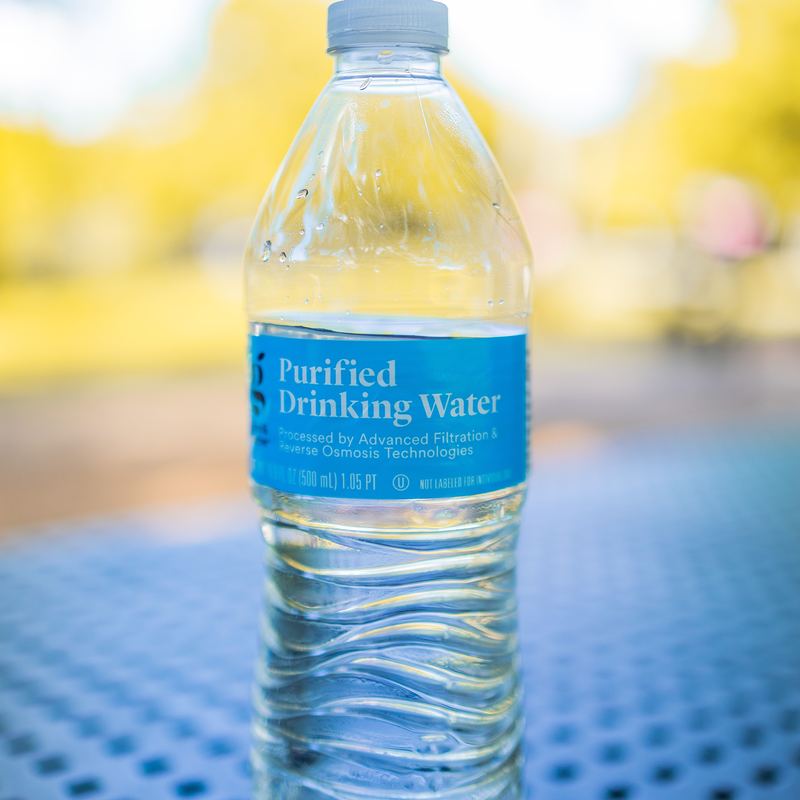 A bottle of cold purified drinking water, sitting on a meshed steel table with a blurred background.