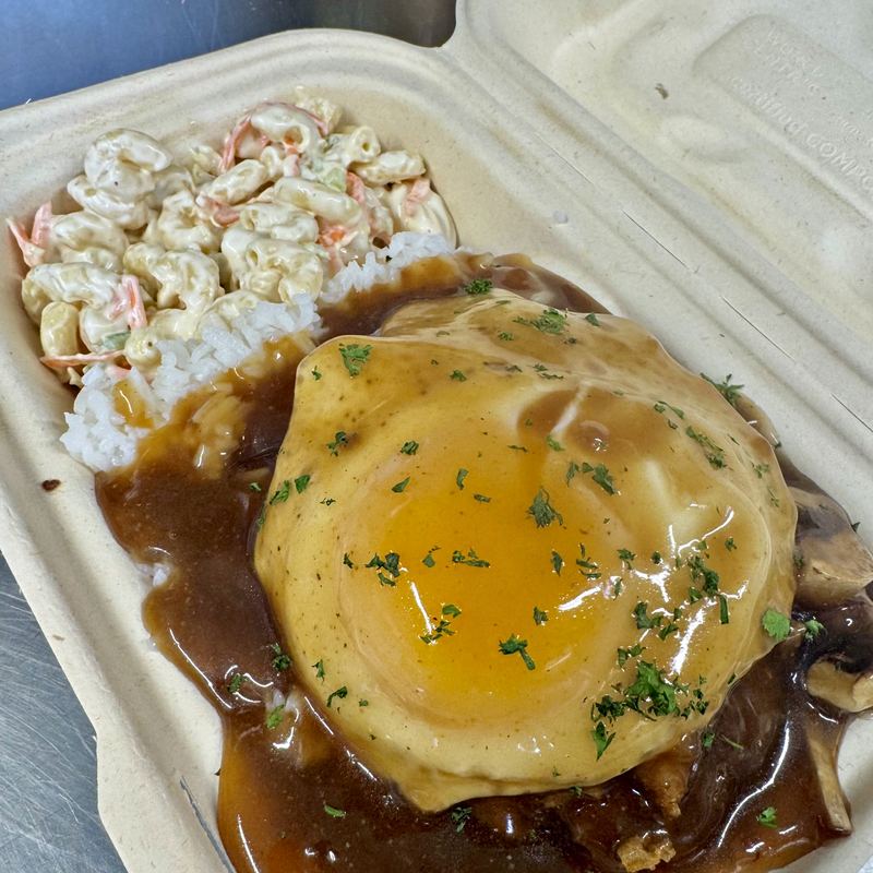 A runny-yolked fried egg covered in brown gravy and scattered herbs sitting on steamed white rice, with macaroni salad on the side.