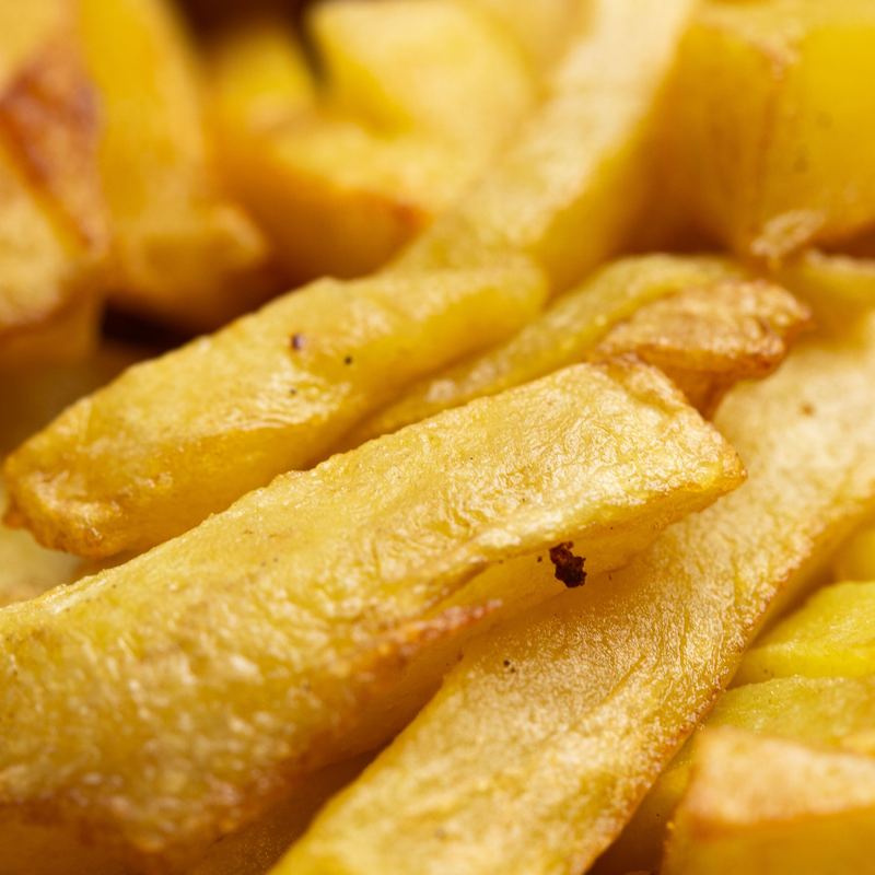 A close view of thick-cut French fries heaped in a pile. The front few are in sharp focus and golden at the crisped edges.