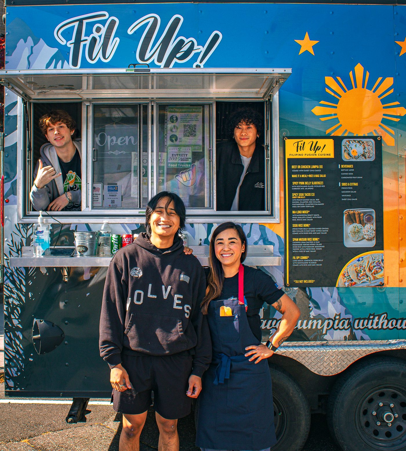 Cayden and Rylan at the Fil Up! serving window while Chef Sarah and Sean (her son) stand in front of the trailer